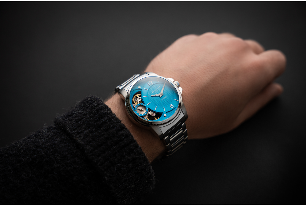 Hand wearing a watch with a blue face on a dark background