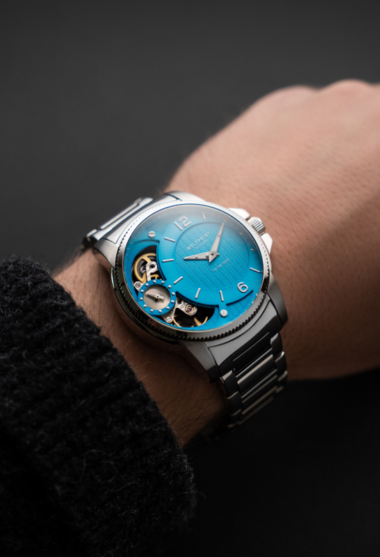 Watch with a blue face and black strap on a wrist against a dark background